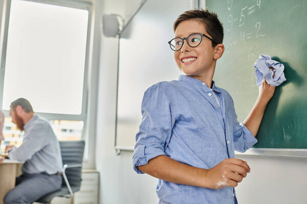 kid stands before a blackboard, smiling in a vibrant classroom setting.