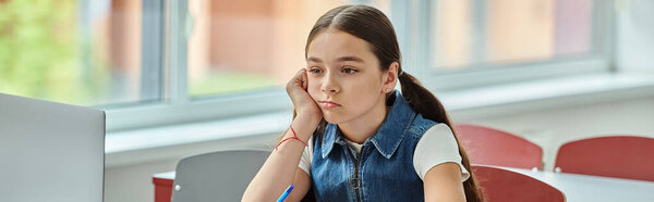 A bored girl sits at a desk, and looking away in classroom