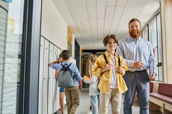 A man teacher energizes a group of kids as they walk down a bright hallway, engaged and eager to learn.