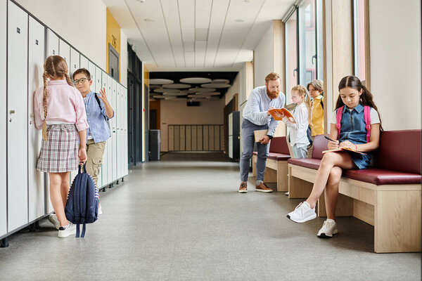 A group of people, including a man teacher, standing in a hallway next to lockers.