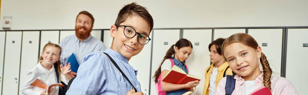 A male teacher is instructing a diverse group of kids in a bright, lively classroom setting. The students are standing next to each other, engaging in learning activities.