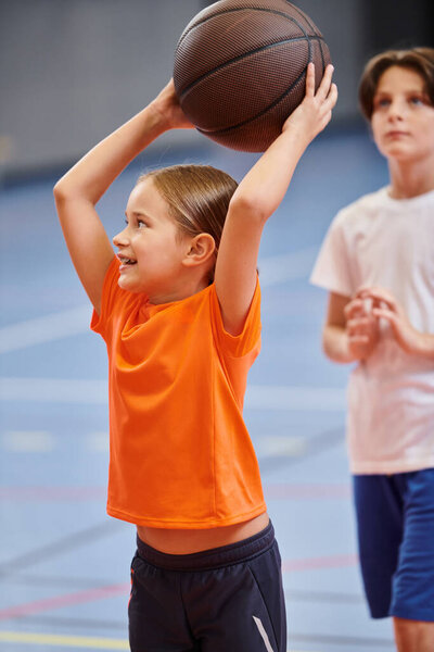 A young girl joyfully holds a basketball high up in the air, radiating a sense of excitement and passion for the game.