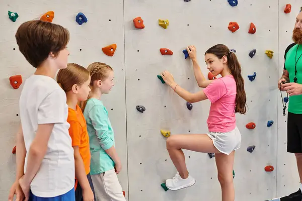 stock image A man teaches a diverse group of children how to climb a rock wall in a vibrant, energetic environment.