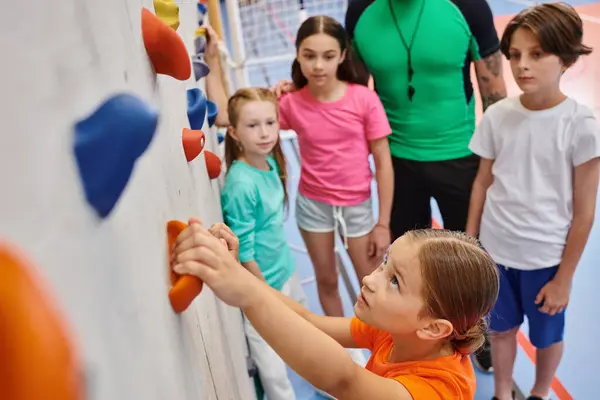 stock image A diverse group of young children stand together, listening attentively to their male teacher in a bright and lively gym.