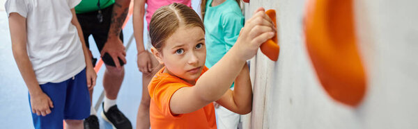 A young girl stands in front of a stark white wall, her presence a contrast to the empty space around her.