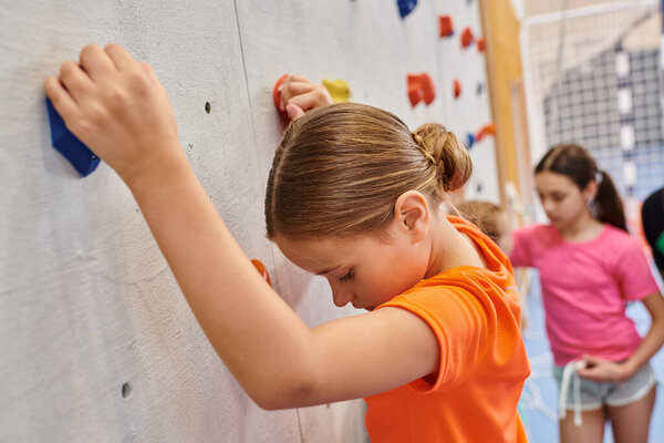 A diverse group of young girls stand side by side, climbing a wall