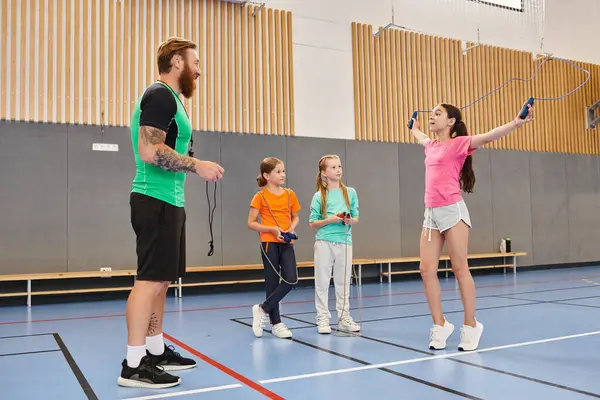 Erkek bir öğretmen tarafından yönetilen çeşitli bir grup çocuk canlı bir sınıfın parlak mavi zemininde güvenle dururlar..