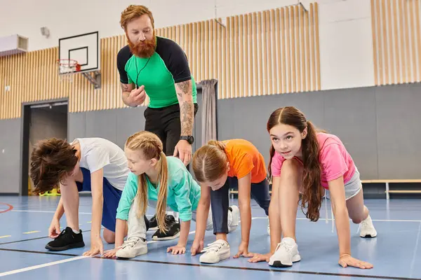 Bir adam tarafından yönetilen çeşitli bir grup çocuk spor salonunda azim ve dikkatle şınav çekiyorlar..