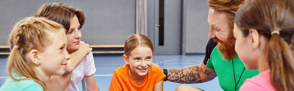 A man teacher is leading a diverse group of kids in an interactive discussion on a colorful court setting, fostering a lively learning environment.