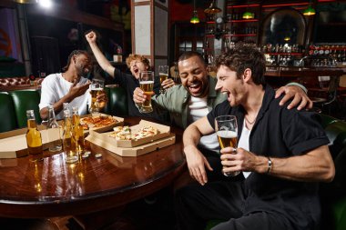 happy interracial male friends laughing and holding glasses of beer in bar, men on bachelor party clipart
