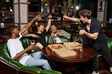 four excited multicultural friends toasting with glasses of beer and spending time together in bar clipart