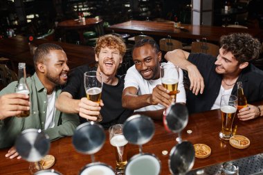 Bekarlığa veda partisinde elinde bira bardakları olan dört heyecanlı etnik erkek, barda erkek arkadaşlar.