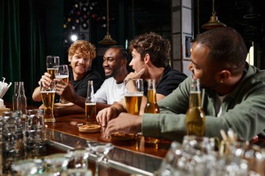 Çok kültürlü erkekler birlikte vakit geçirir, sohbet eder ve birayla kadeh kaldırır, barda erkek arkadaşlar