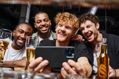 Barda bekarlığa veda partisi sırasında akıllı telefondan selfie çeken ve bira içen pozitif ırklar arası erkekler.