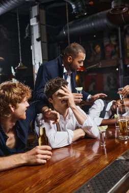 drunk man with tie on head covering face while listening to friend after drinking tequila and beer clipart