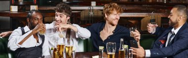 banner of happy multicultural friends drinking whiskey near tequila shots and beer on table in bar clipart