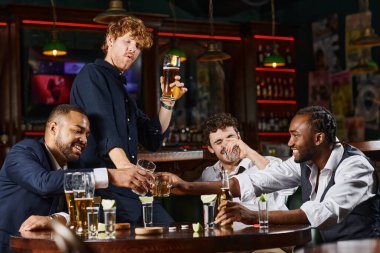 cheerful and drunk multiethnic colleagues toasting with glasses of whiskey after work in bar clipart