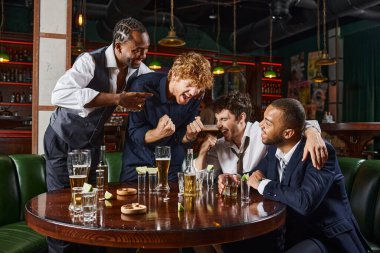 Sarhoş ırklar arası arkadaşlar işten sonra barda rahatlarken gülüyor ve alkol içiyorlar.