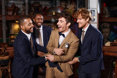 bachelor party, excited interracial men congratulating friend in bar, best men and groom in suits clipart