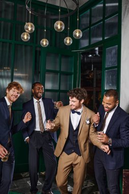 bachelor party, interracial best men and groom laughing while standing with glasses of whiskey clipart