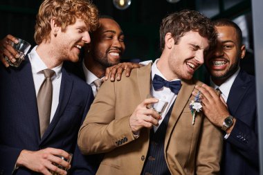 bachelor party, excited multiethnic best men and groom laughing in bar, holding glasses of whiskey clipart