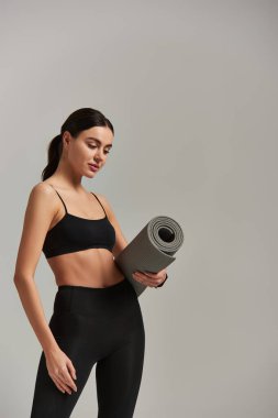 Genç formda spor kadın tozluklu ve etekli üstte spor minderi ve gri arka planda duruyor.