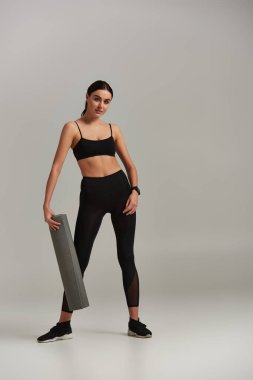 Aktif giyinen, spor elbiseli, spor ayakkabılı ve gri arka planda duran bir kadın.