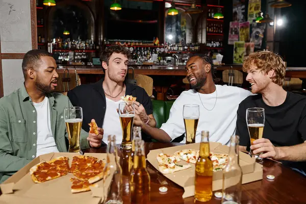 group of four interracial friends eating pizza and drinking beer in bar, men during bachelor party