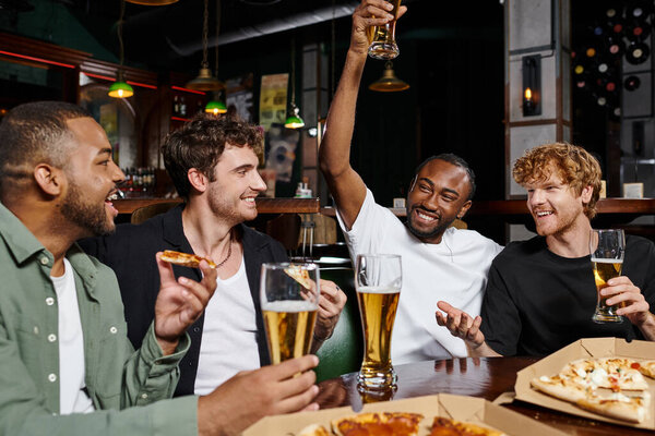 happy african american man raising glass of beer near interracial friends during bachelor party