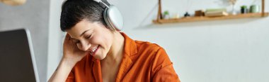 joyous female student in orange shirt with headphones studying at her laptop, education, banner clipart