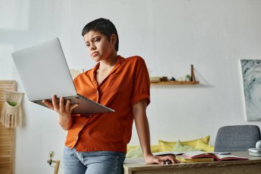 Elinde dizüstü bilgisayarlarla masanın yanında duran ciddi bir öğrenci.