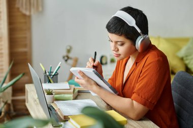 young female student studying hard and taking notes while on remote lesson, education at home clipart