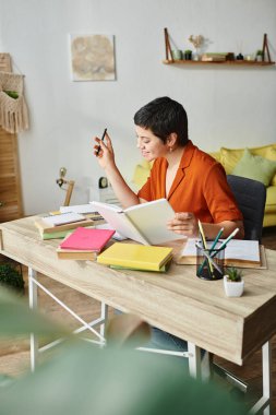 vertical shot of cheerful young woman in orange shirt smiling happily while studying hard, education clipart