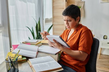 confused short haired female student in orange shirt looking at her textbook while studying hard clipart