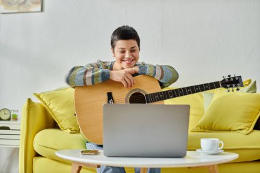 Çevrimiçi gitar dersi sırasında dizüstü bilgisayara gülümseyen neşeli genç kadın, evde sanal eğitim