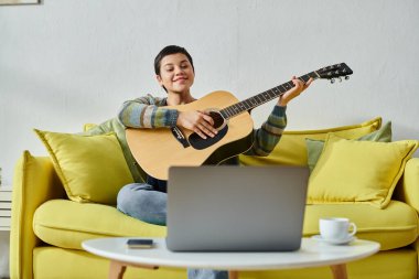 Günlük ev kıyafetleri içinde neşeli çekici bir kadın online gitar dersine katılıyor, evde eğitim görüyor.