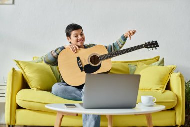 Genç, neşeli bir kadın, gündelik kıyafetleriyle koltukta oturuyor ve uzak bir sınıfta gitar çalmayı öğreniyor.