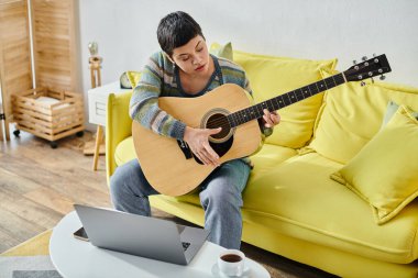 Konsantre genç kadın koltukta oturup gitar çalışıyor uzaktan müzik dersi, eğitim.