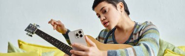 Elinde telefon, eğitim ve afişle online gitar kursuna katılan çekici bir kadın.
