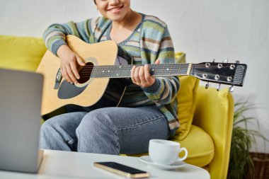 Laptopun önünde oturan genç bir kadının uzaktan kumandalı sınıfta gitar çalmayı öğrenmesi.