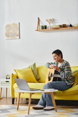 Uzaktan gitar dersi alan gülen genç bir kadının kanepede oturduğu, evde eğitim gördüğü dikey bir fotoğraf.