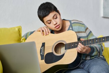 Yoğunlaşmış genç bir kadın gitar çalmayı uzaktan müzik dersi ve evde eğitim alarak öğreniyor.
