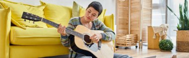 Gitarlı genç bir kadın online müzik dersinde yerde oturuyor, evde eğitim, pankart