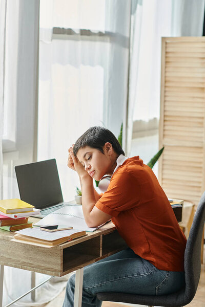 vertical shot of young pensive student sitting at table while attending online class, education