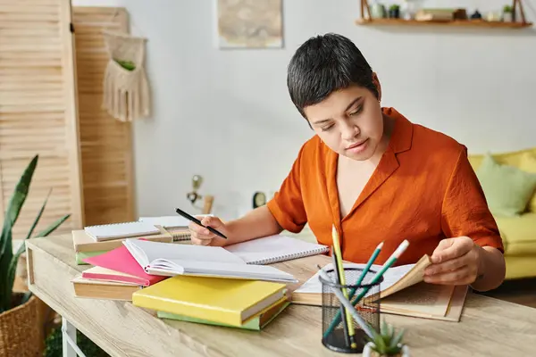 穿着橙色衬衫的勤勤恳恳的年轻学生 写笔记 看课本 在家接受教育 — 图库照片
