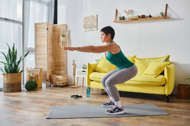 Spor kıyafetleri içinde çekici bir kadın. Önünde elleri, spor ve spor kıyafetleri ile çömeliyor.