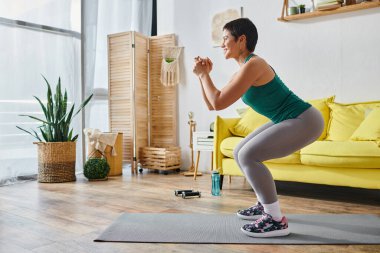 Güzel görünüşlü, spor kıyafetli, elleri önünde, spor ve spor kıyafetleri içinde, çömelmiş bir kadın.
