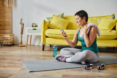 Spor giyim sektöründe neşeli, çekici bir kadın spor yaptıktan sonra cep telefonuna gülümsüyor.