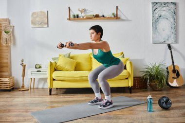 Atletik kısa saçlı, dövmeli, önünde dambılları olan, spor ve spor yapan bir kadın.
