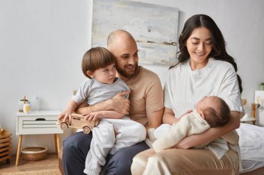 Güzel, modern bir aile rahat bir ev elbisesi içinde yatakta oturuyor ve neşeyle gülümsüyor, aile kavramı.